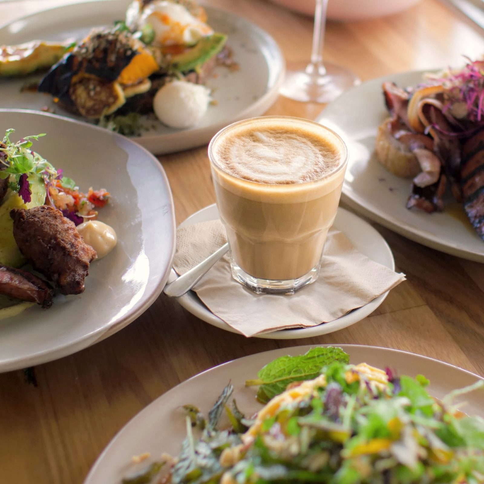 Brunch plates and a glass latte on a timber table