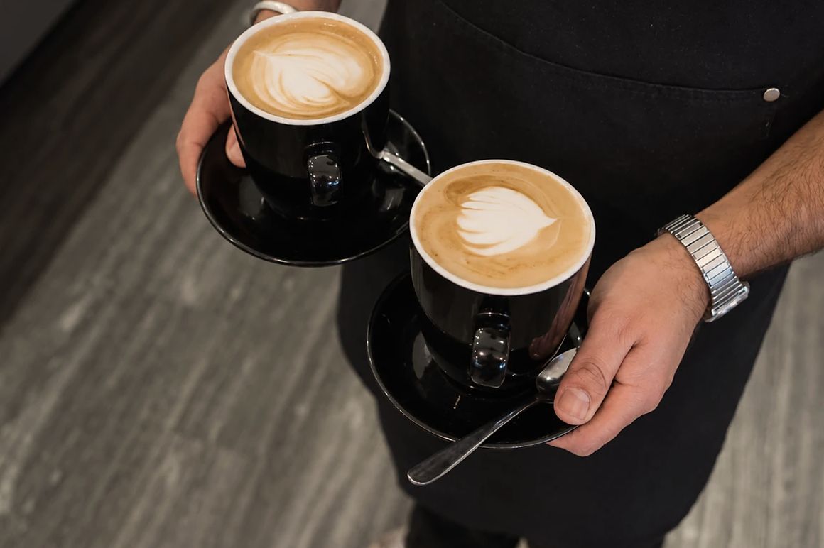 Two lattes with leaf art carried on their saucers by an Oar barista