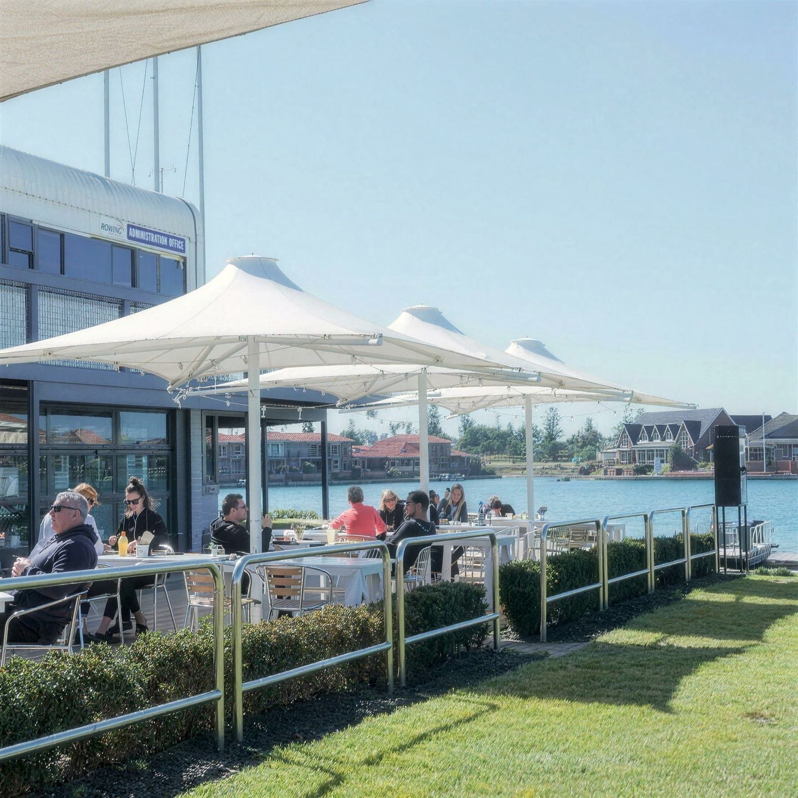 Tables under the white sails on the deck at Oar, beside the lawn and the lake