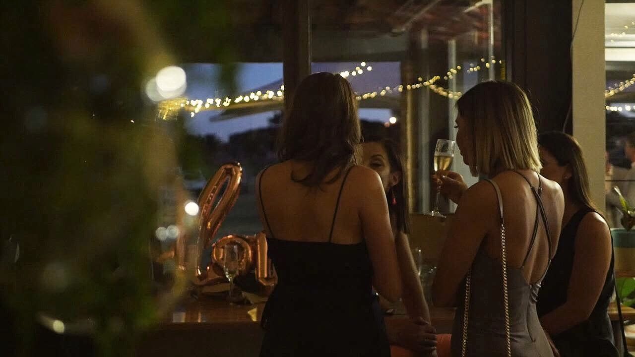 Guests with champagne at an evening birthday party at Oar, with fairy lights over the lake behind them